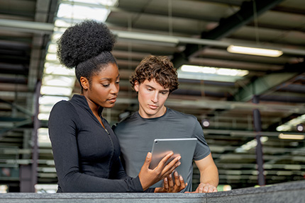 Trainerin erklärt einem Azubi etwas an einem Tablet.