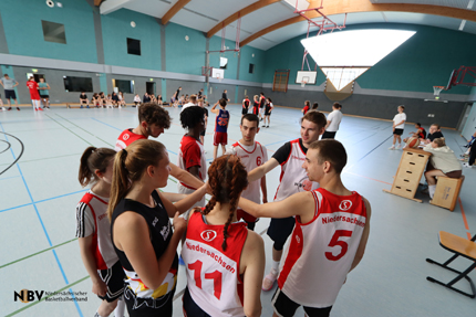 Basketballspieler und -spielerinnen stehen im Kreis und schlagen in der Mitte die Hände zusammen