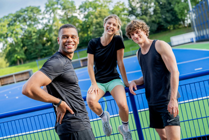 Eine Sportlerin und zwei Sportler lachen in die Kamera.