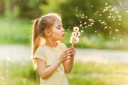 Mädchen pustet gegen eine Pusteblume/Löwenzahn